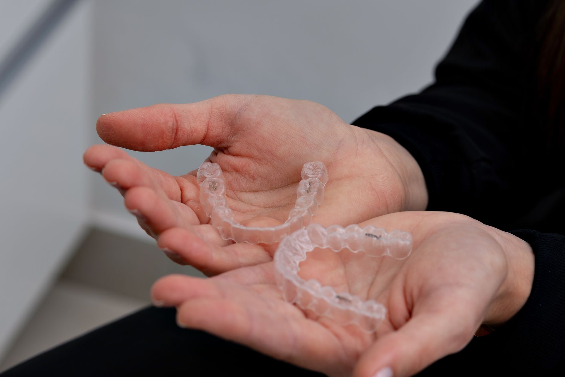 Hands holding a set of clear dental aligners in a modern dental office.