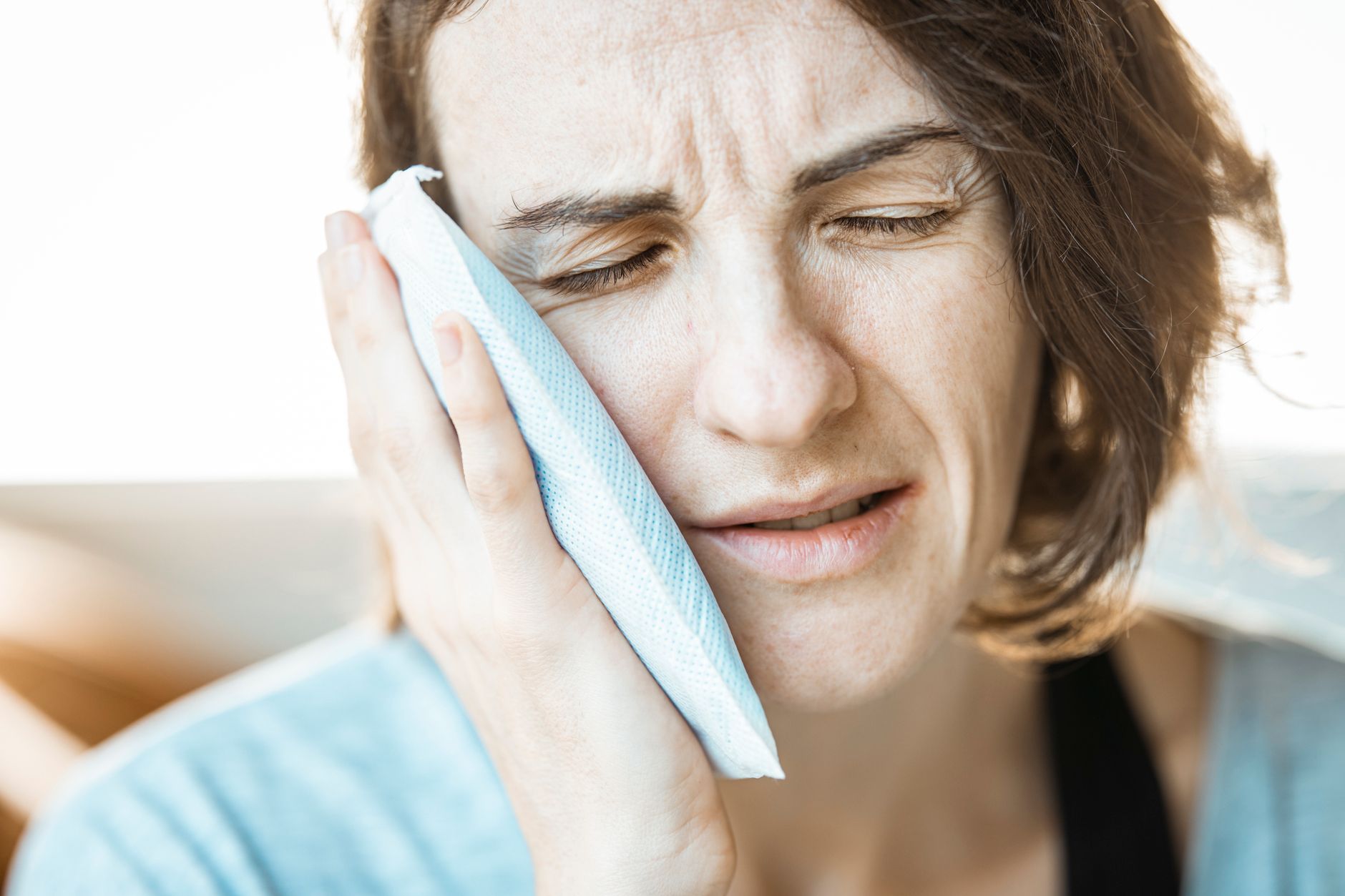 A woman in discomfort applying a cold compress to her cheek for relief from jaw and facial pain.